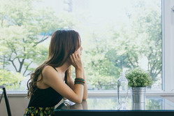  A young woman is sitting at a table and peering to the front. There is a flower pot and a bottle of water on the table. She will be afraid of the nature including plants and water in the future. 
