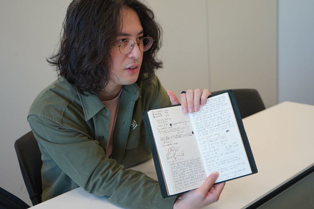 人工言語のアイデアが書かれたノートを手に取る中野さん