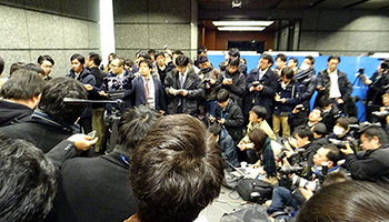 報道陣に囲まれながら、事業継続の意思はあると強調した大塚COO（左端）