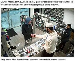 ショーケースの前でスマホを見ていた男（画像は『The Sun　2022年12月6日付「ESCAPE’S CUT OFF Moment bungling thief tries to flee shop with stolen phones ― but can’t open the DOOR」（Credit: SWNS）』のスクリーンショット）