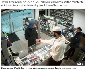 ショーケースの前でスマホを見ていた男(画像は『The Sun 2022年12月6日付「ESCAPE’S CUT OFF Moment bungling thief tries to flee shop with stolen phones ― but can’t open the DOOR」(Credit: SWNS)』のスクリーンショット)